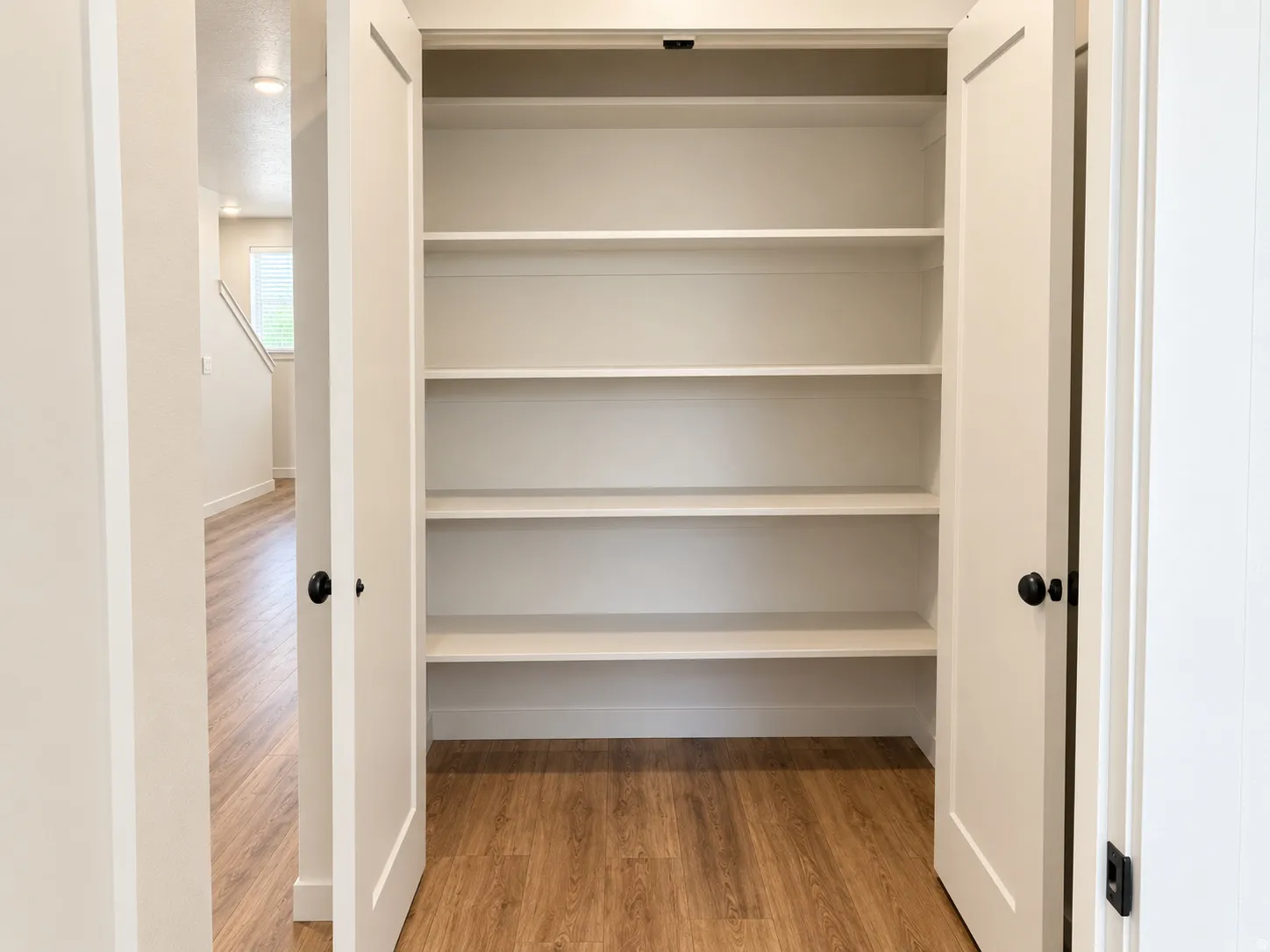 Built-in shelving unit with multiple white shelves, paneled double doors, and black hardware