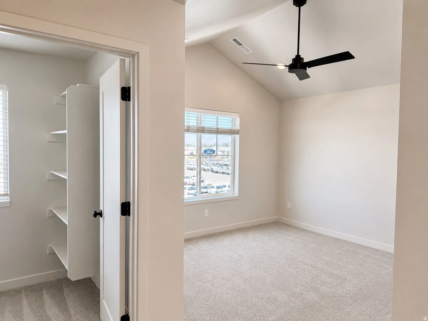 Vaulted ceiling room featuring a modern black ceiling fan, light neutral carpeting, and a large window with blinds