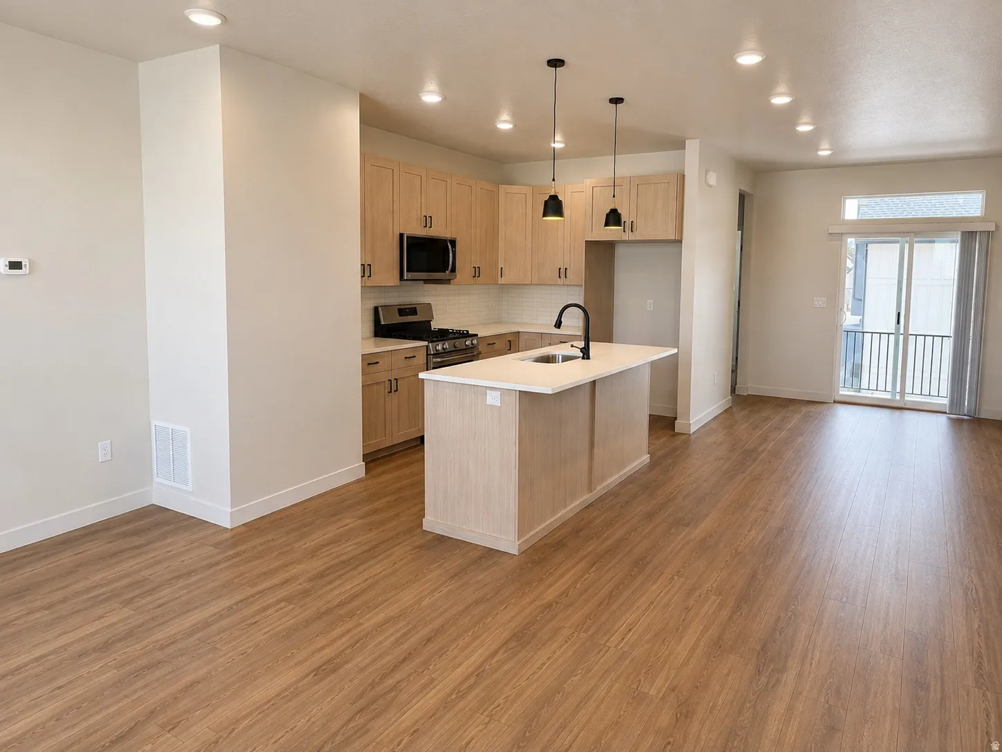 Open-concept living space with wood-finish flooring, recessed lighting, and a sliding glass door to an exterior balcony