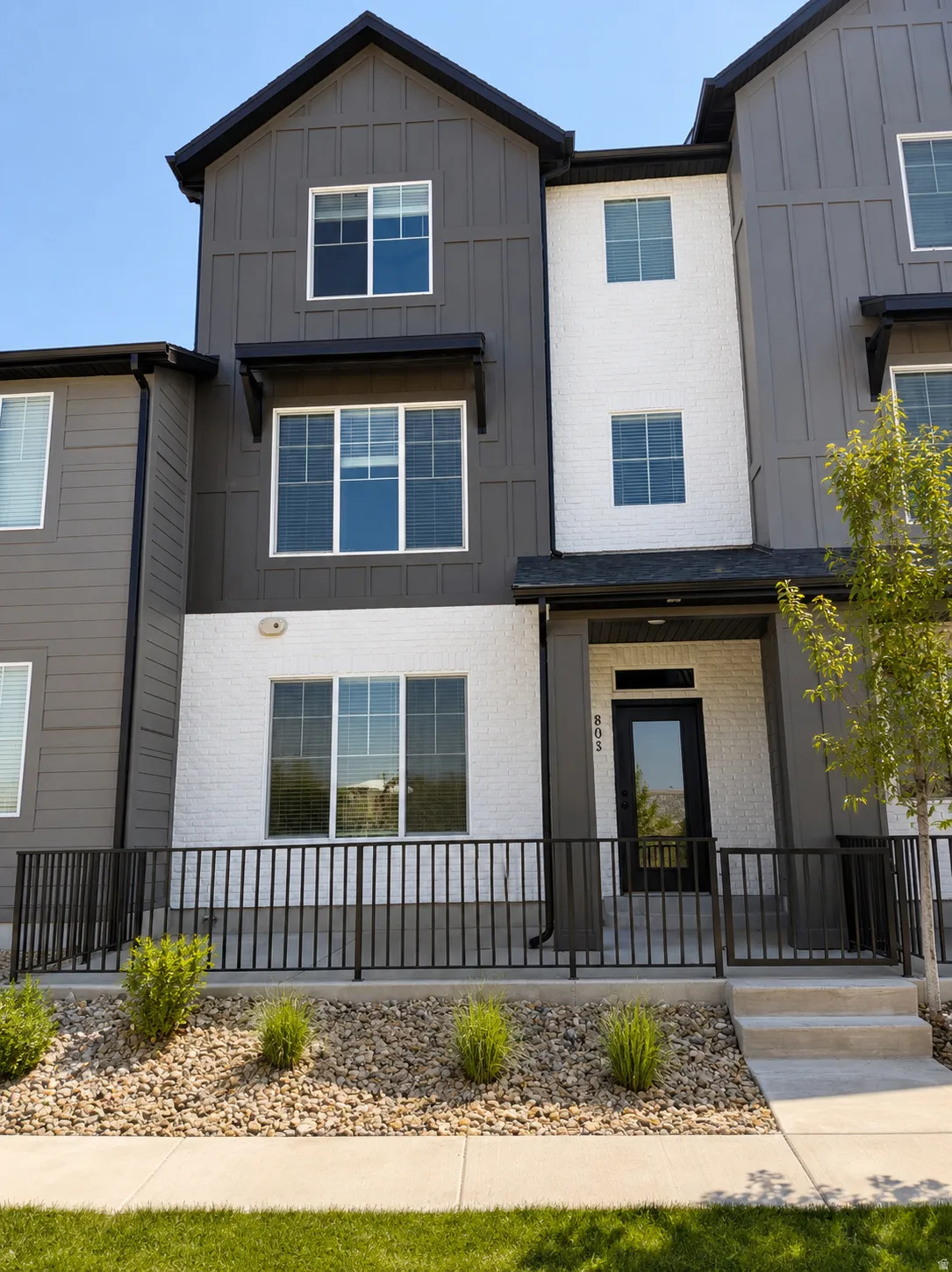 Modern townhome exterior featuring vertical board and batten siding, white brick accents, and black trim