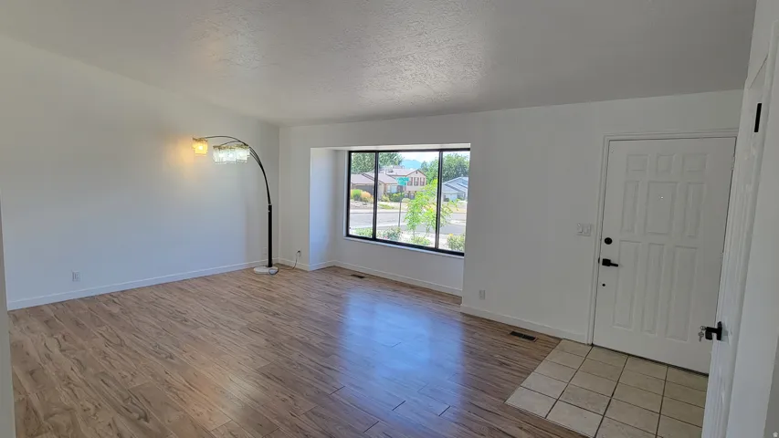 Expansive living area with wood-finish flooring, a large picture window, and a paneled entry door