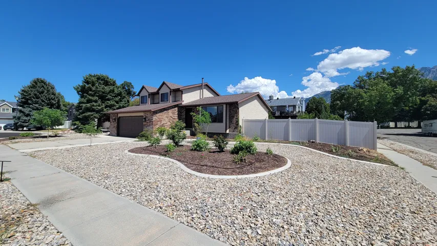 Brick and stucco exterior with multiple gables, an attached garage, and a gravel front yard with landscaped beds