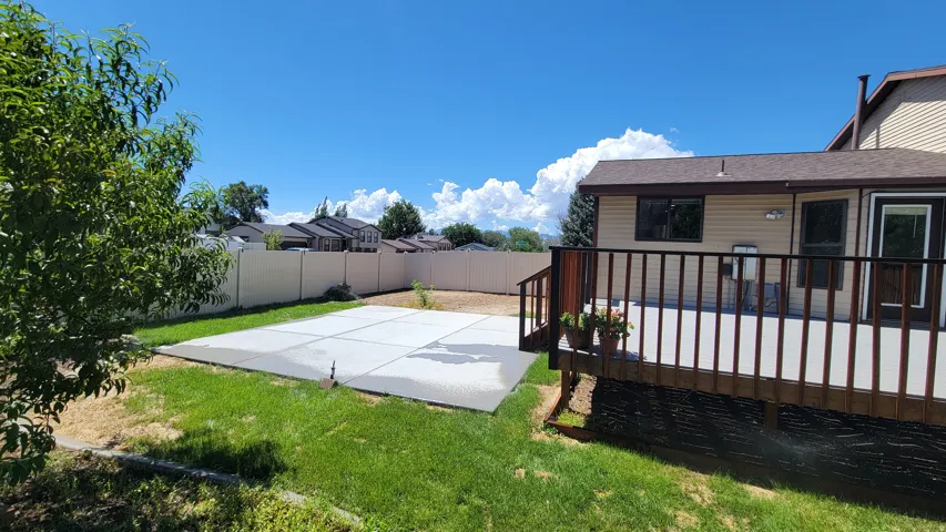 Spacious backyard featuring a large concrete patio, a wood-finish deck with railing, and perimeter fencing