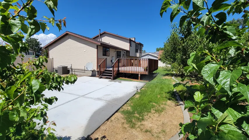 Rear exterior featuring a wood deck, concrete patio, and mature landscaping