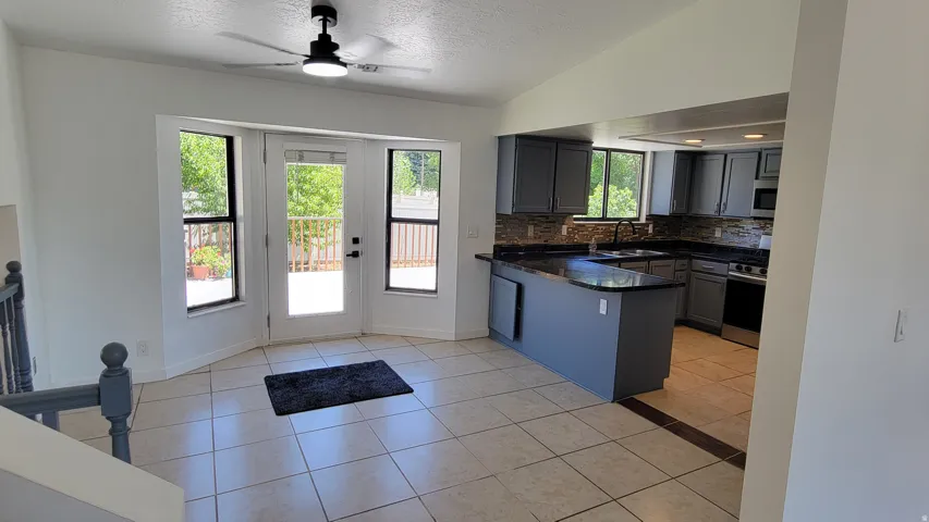 Tiled flooring, bay window with French doors, kitchen with gray cabinetry, dark countertops, and stainless steel appliances