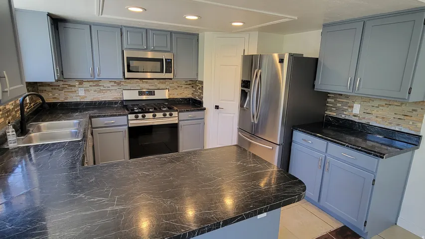 Kitchen featuring slate blue cabinetry, dark countertops, a mosaic tile backsplash, and stainless steel appliances