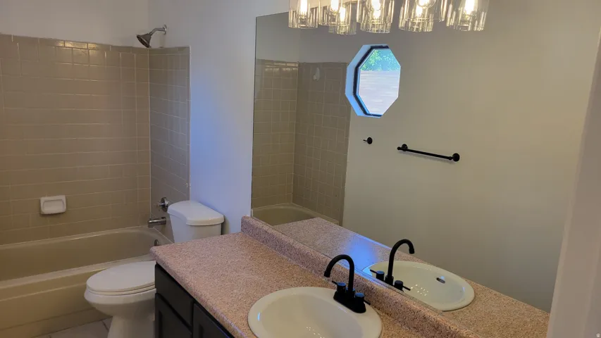 Double vanity with matte black fixtures, octagonal window, tub/shower combination with tiled surround, and updated light fixture