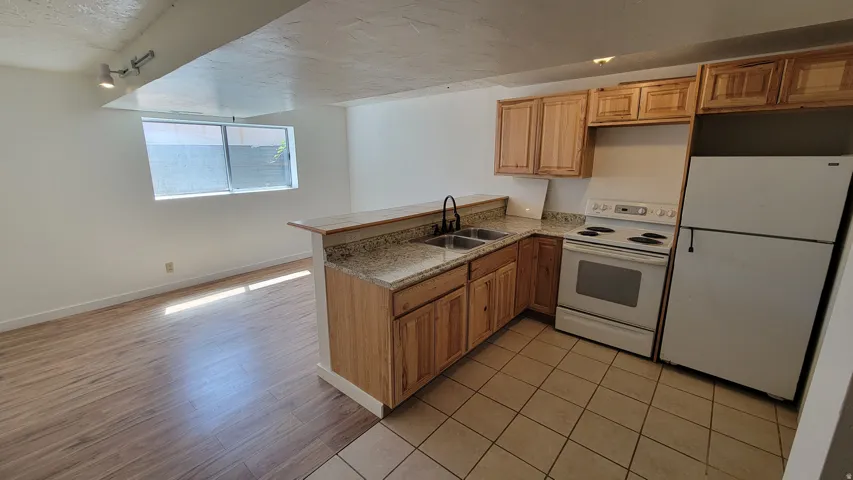Kitchen with wood cabinetry, granite-style countertops, stainless steel dual basin sink, and white appliances