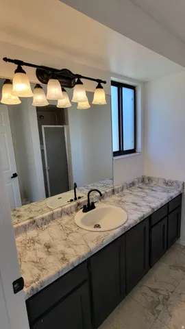 Bathroom featuring a wide vanity with a patterned countertop, dual-basin sink, and black fixtures