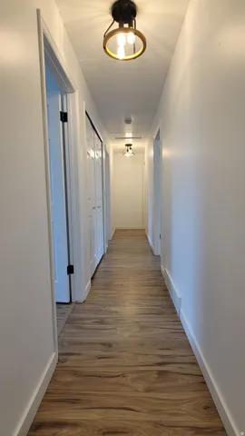Hallway featuring wood-finish flooring, white walls, and contemporary ceiling light fixtures