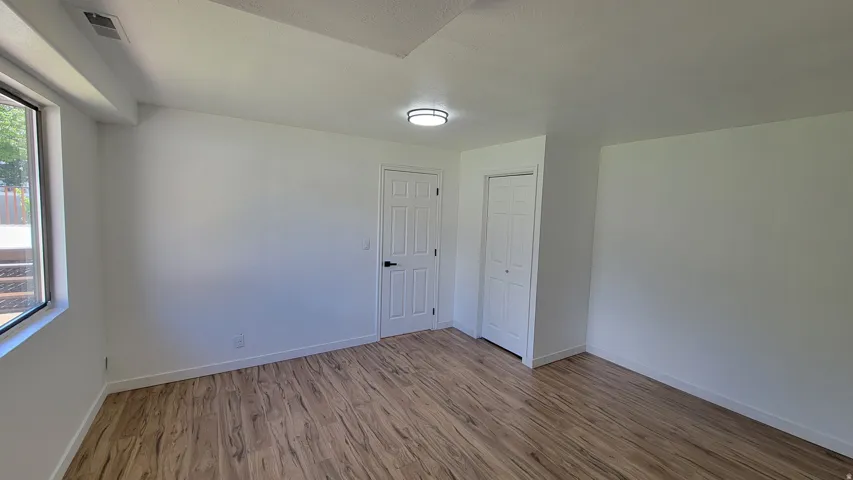 Wood-finish flooring, white walls, overhead ceiling light fixture, white interior doors, and a window