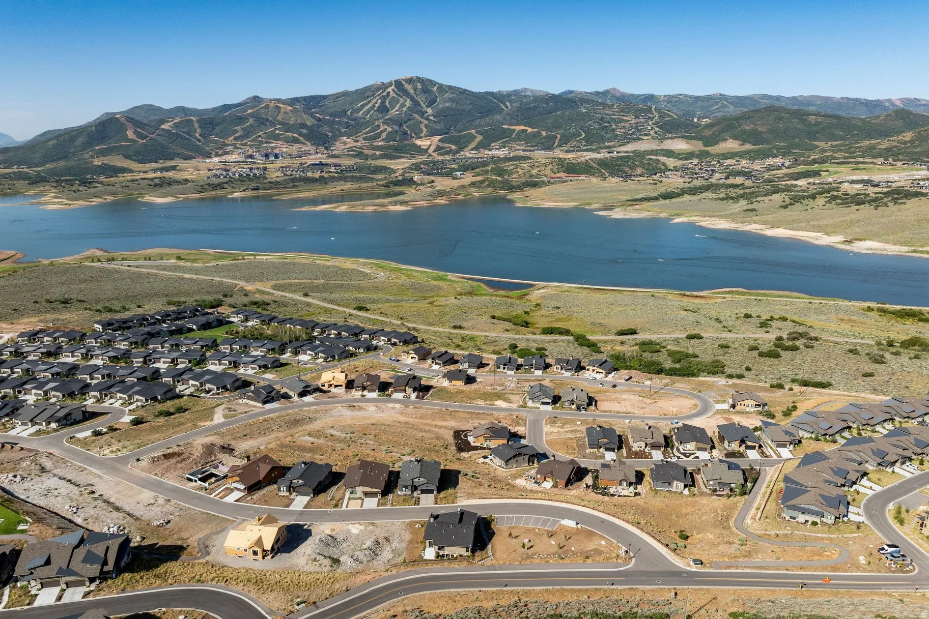 Newly constructed residential community with modern homes featuring tan and earth-tone exteriors, situated on rolling terrain overlooking a scenic reservoir