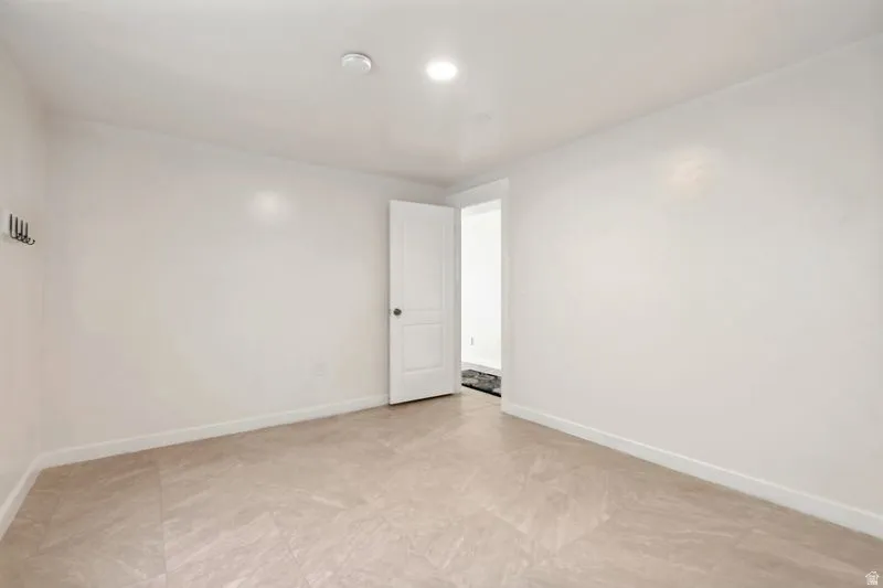 Spacious room featuring light-toned tile flooring, recessed lighting, white baseboards, a white interior door, and a wall-mounted coat rack