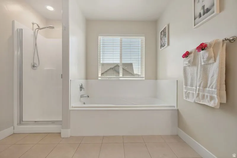 Bathroom featuring a built-in tub, a separate enclosed shower with a glass door, a window with horizontal blinds, recessed lighting, and tile flooring
