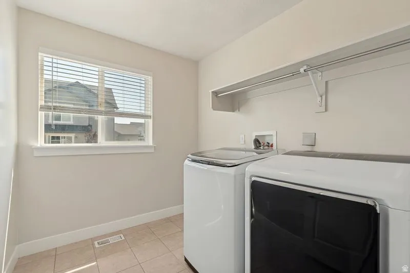 Dedicated laundry room featuring side-by-side washer and dryer appliances, tile flooring, ample counter space with stainless steel rod, and natural light from a double-hung window with plantation shutters
