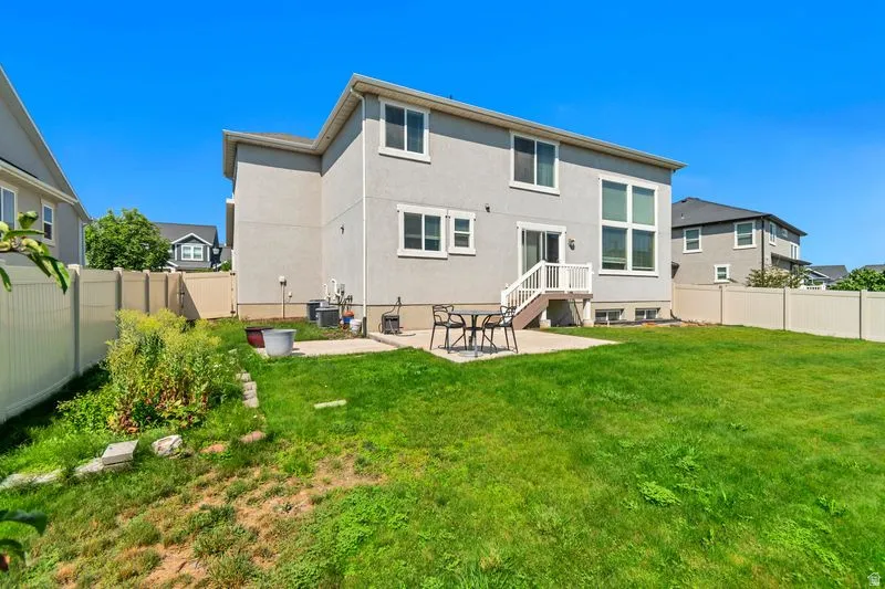 Expansive backyard featuring a green lawn, concrete patio, and a privacy fence