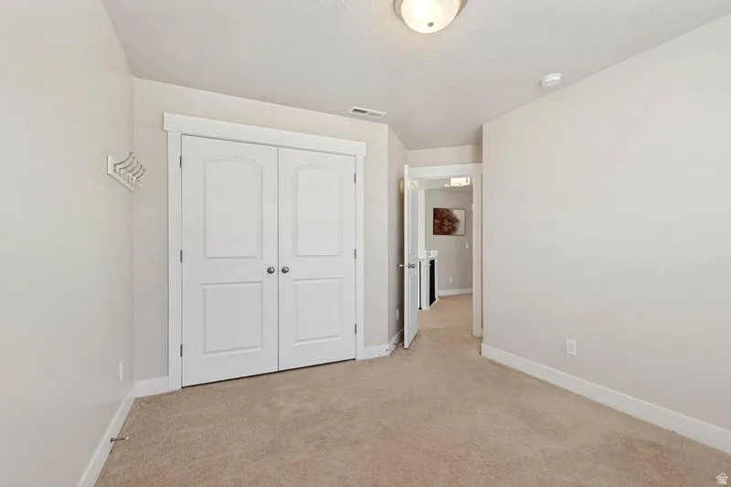 Spacious bedroom featuring neutral carpeting, white double-panel closet doors with six-panel design, ceiling-mounted lighting fixture, and clean white walls throughout