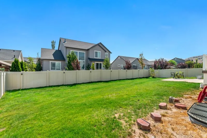 Expansive backyard featuring a generously sized manicured lawn bordered by vinyl fencing, mature landscaping with established trees and shrubs, and a level yard ideal for outdoor recreation and entertaining