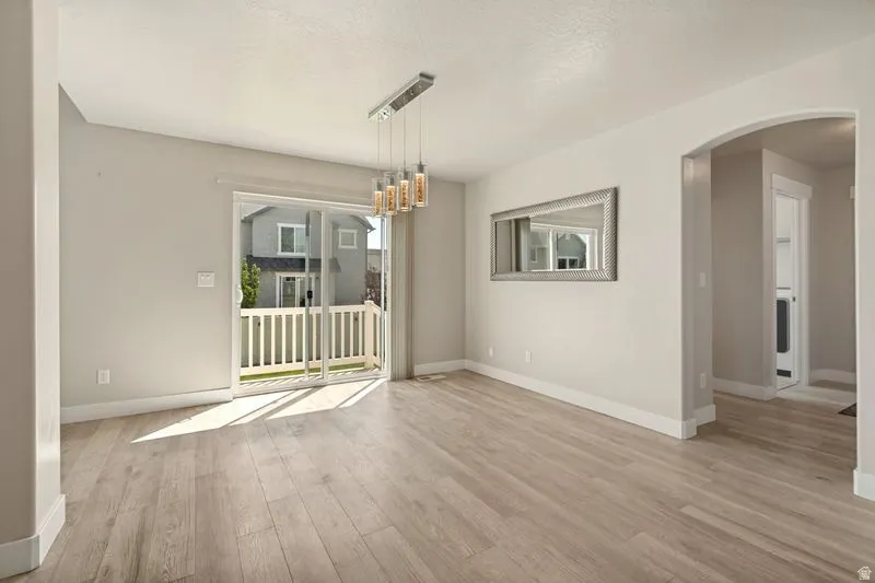 Bright and spacious living area showcasing gleaming wood-finish flooring, abundant natural light from expansive glass doors, and a modern pendant light fixture