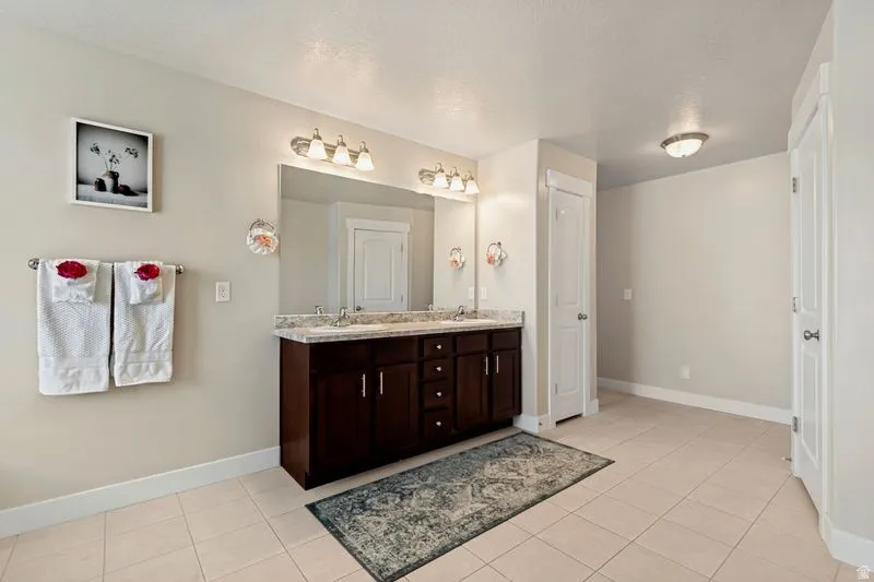 Spa-inspired primary bathroom featuring a dark wood dual-vanity with ample storage, marble-style countertops, and an oversized framed mirror with integrated lighting