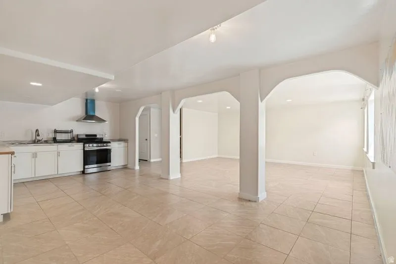 Open-concept living space featuring neutral tile flooring, white cabinetry, a stainless steel range with a coordinating hood, and multiple arched doorways