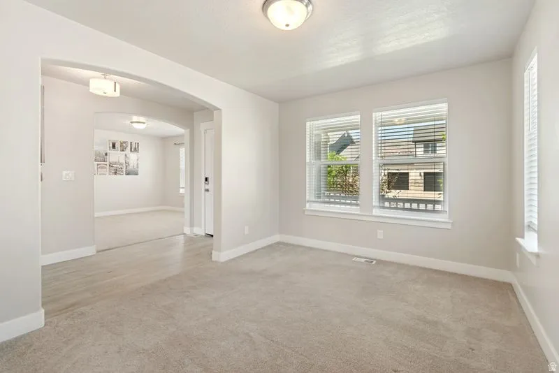 Spacious room featuring neutral carpeting, multiple windows with blinds, and an arched entryway