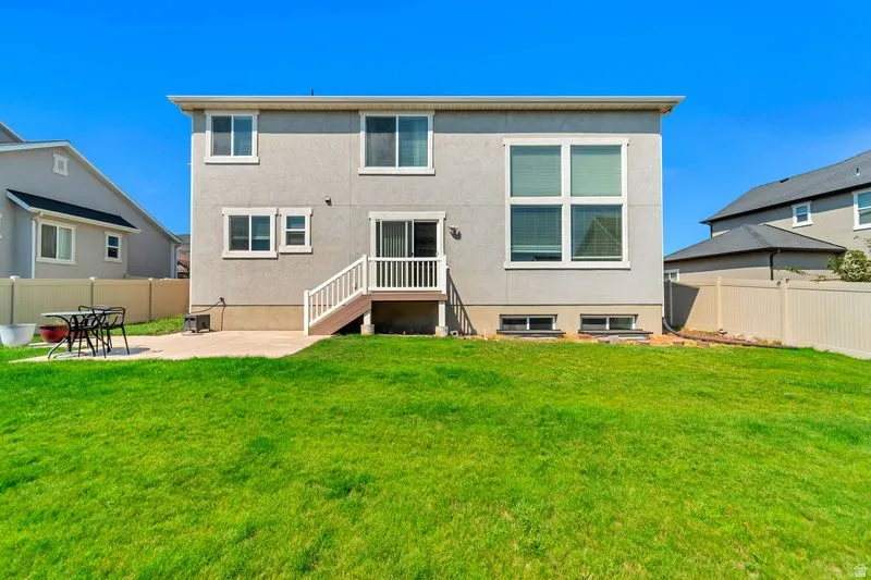 Expansive backyard featuring a manicured lawn, a concrete patio, and a two-story residence with a stucco exterior