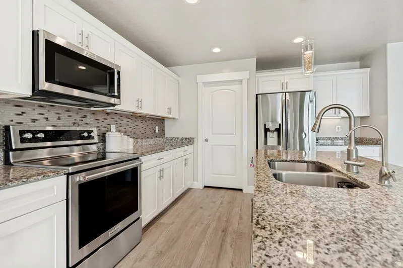 Kitchen featuring white cabinetry, granite countertops, stainless steel appliances, a tiled backsplash, and wood-finish flooring