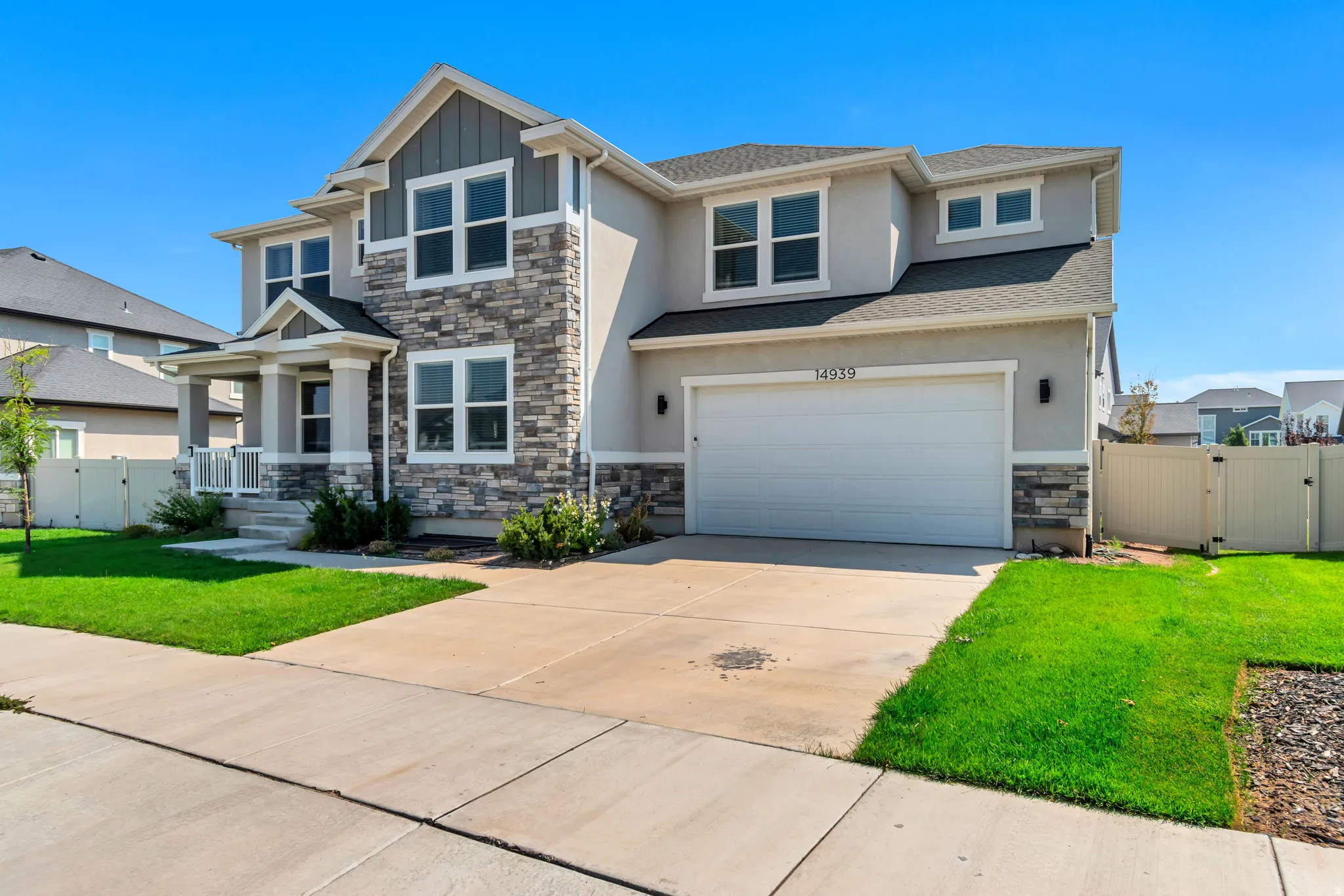 Two-story residence featuring a stone and stucco facade, a covered front porch, and a two-car garage with an asphalt driveway