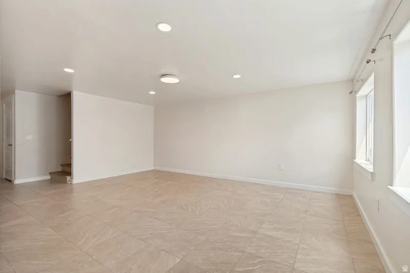 Spacious room featuring tile flooring, white baseboards, recessed lighting, and a modern ceiling light fixture