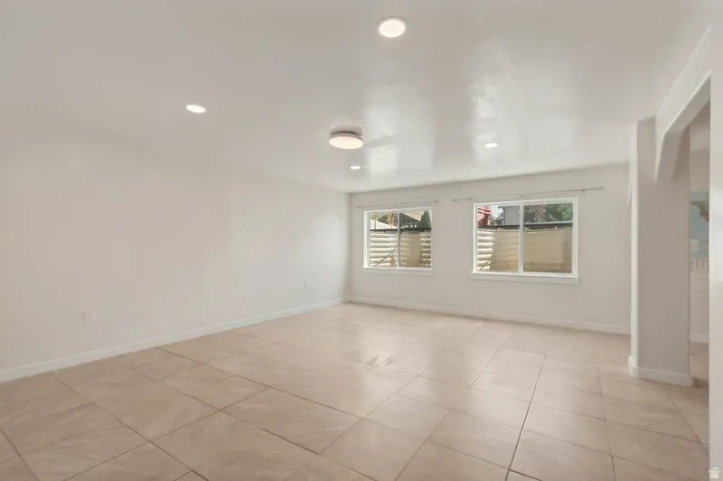 Spacious room featuring neutral-toned tile flooring, recessed lighting, and two windows