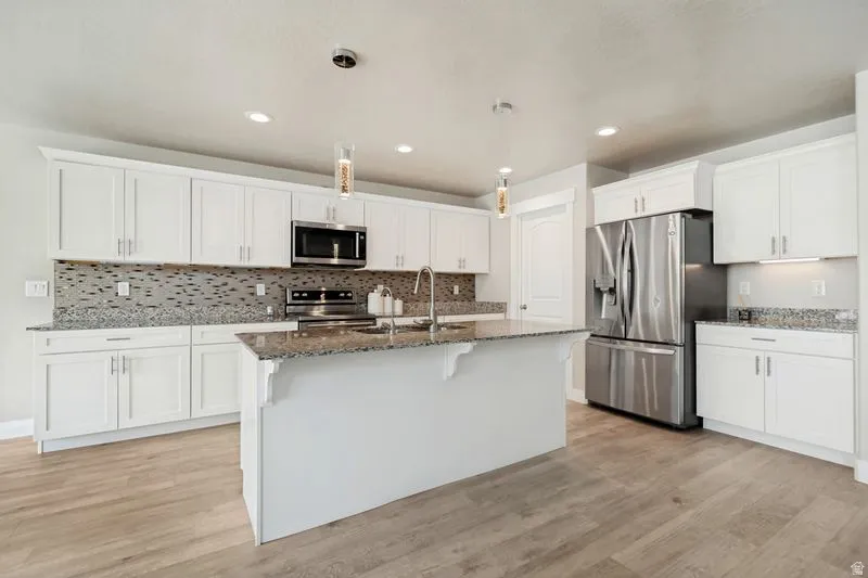 Kitchen featuring an island, white cabinetry, integrated stainless steel appliances, granite countertops, and wood-finish flooring