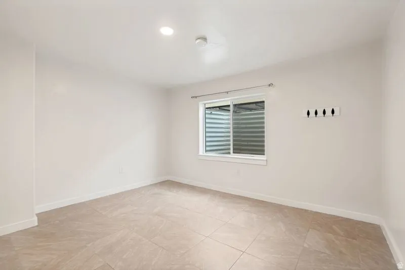 Spacious room featuring light-colored tile flooring, white walls, and a window with a window well