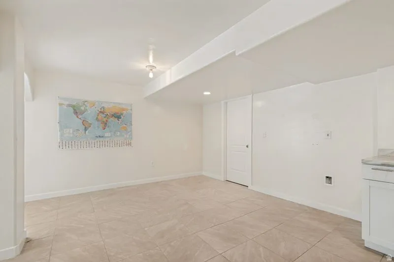 Spacious room featuring neutral tile flooring, recessed lighting, white walls, and a built-in cabinet with a stone-finish countertop