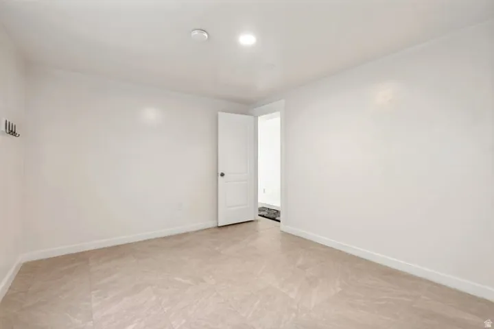 Spacious room featuring light-toned tile flooring, recessed lighting, white baseboards, a white interior door, and a wall-mounted coat rack