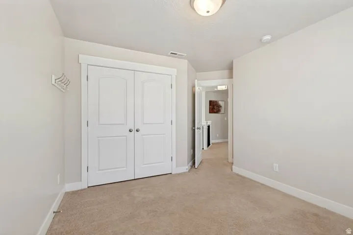 Spacious bedroom featuring neutral carpeting, white double-panel closet doors with six-panel design, ceiling-mounted lighting fixture, and clean white walls throughout