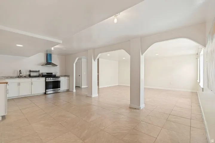Open-concept living space featuring neutral tile flooring, white cabinetry, a stainless steel range with a coordinating hood, and multiple arched doorways