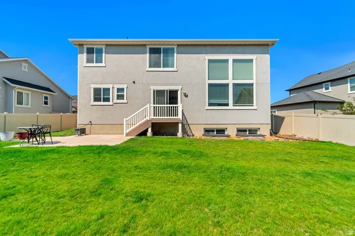 Expansive backyard featuring a manicured lawn, a concrete patio, and a two-story residence with a stucco exterior