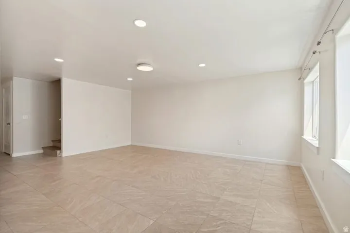 Spacious room featuring tile flooring, white baseboards, recessed lighting, and a modern ceiling light fixture