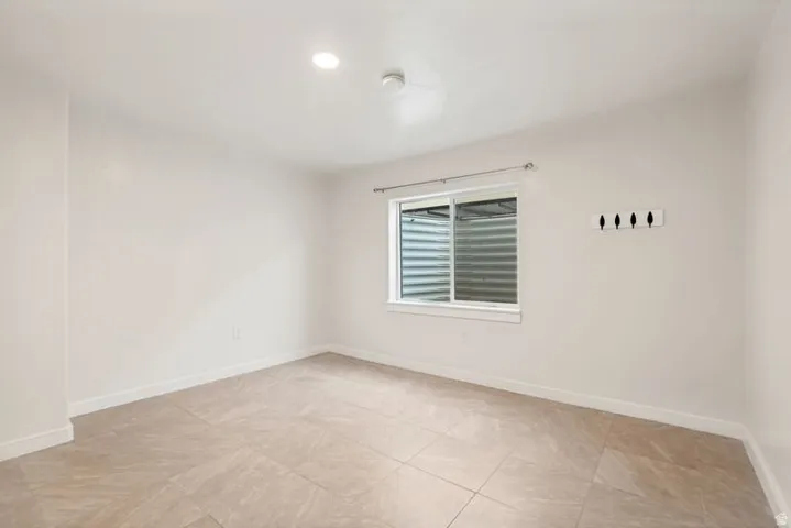 Spacious room featuring light-colored tile flooring, white walls, and a window with a window well