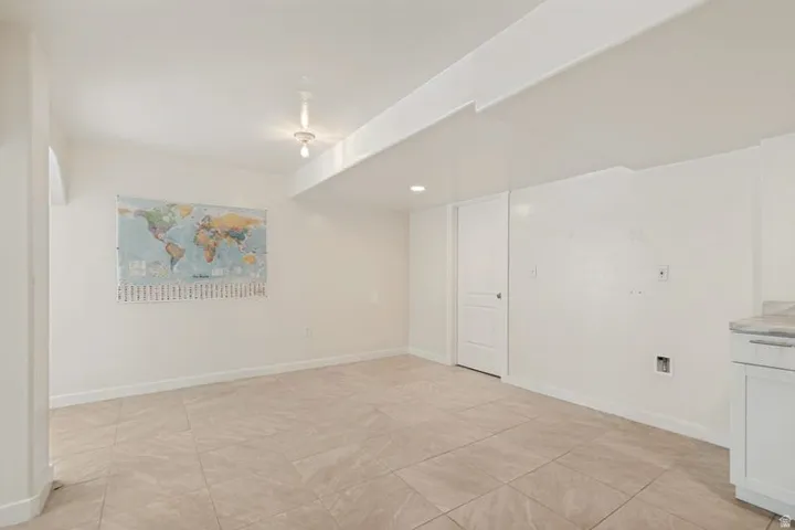 Spacious room featuring neutral tile flooring, recessed lighting, white walls, and a built-in cabinet with a stone-finish countertop
