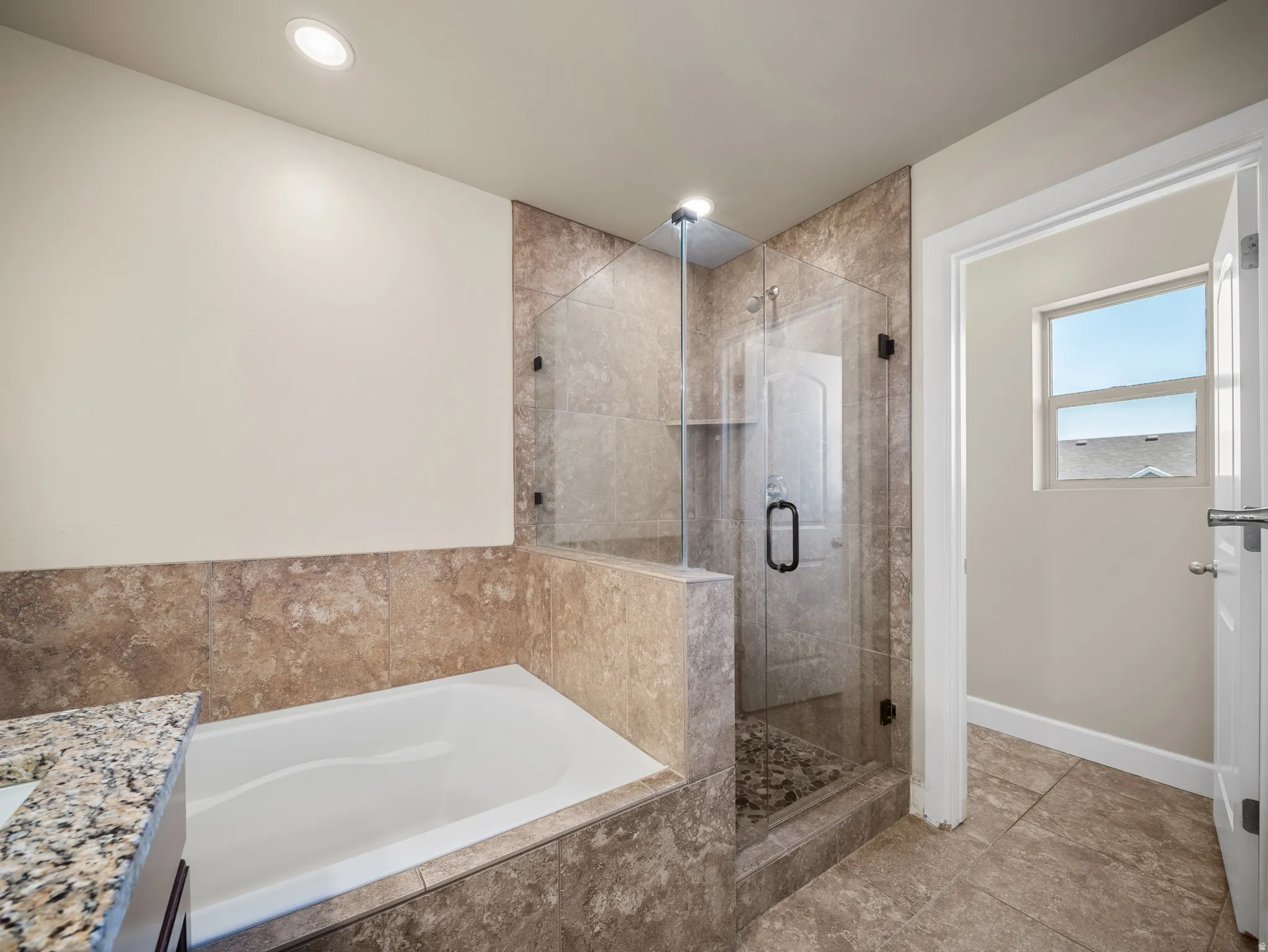 Bathroom featuring a glass-enclosed shower with pebble-finish flooring, a built-in bathtub, and stone-finish wall tiling
