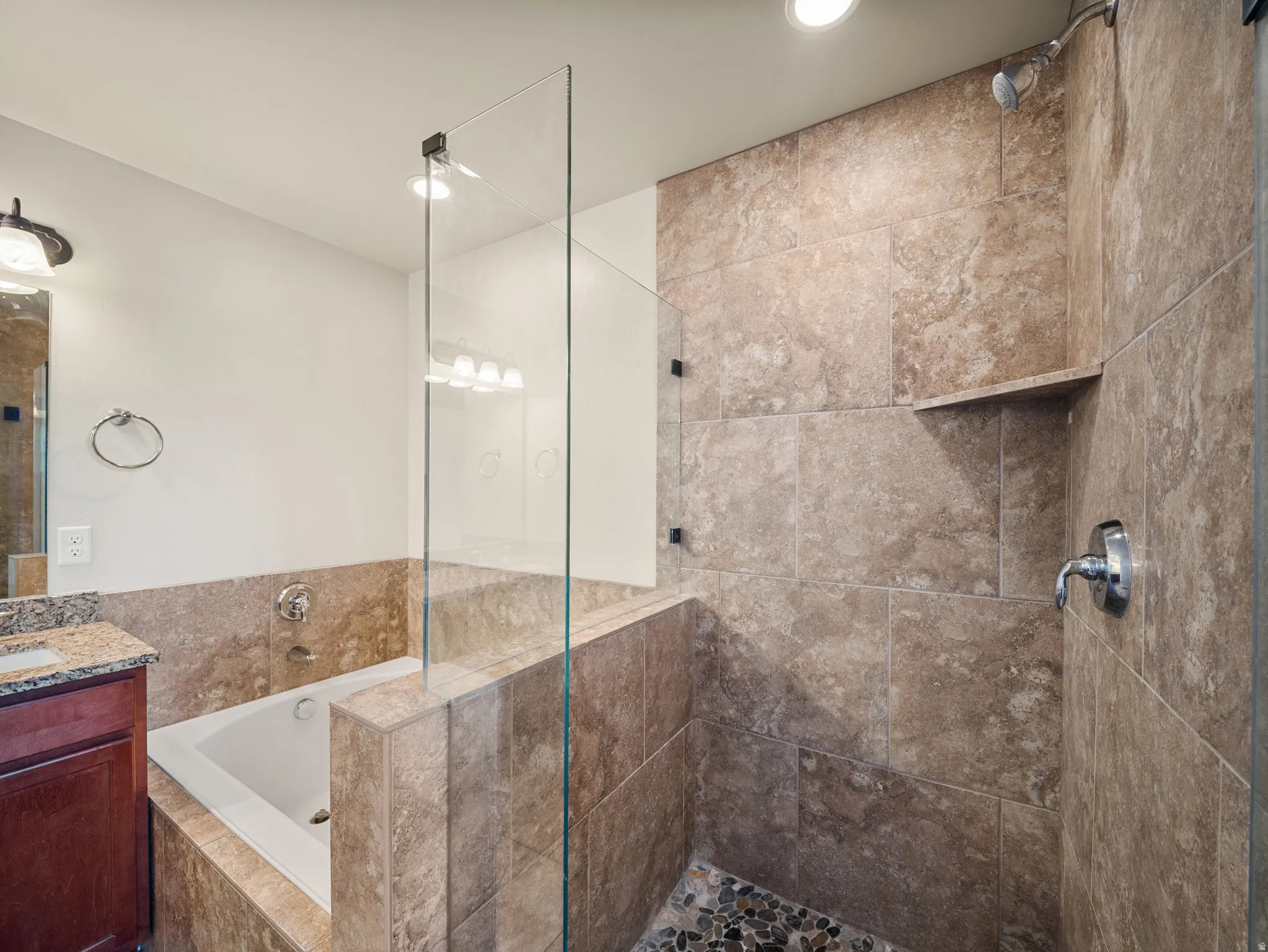 Bathroom featuring a tiled walk-in shower with a built-in shelf, a separate soaking tub, and a vanity with a granite-style countertop