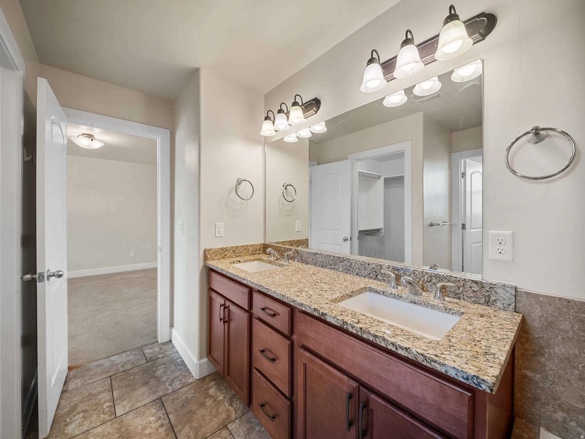 Double vanity with integrated sinks, granite countertop, wood-finish cabinetry, and sconce lighting