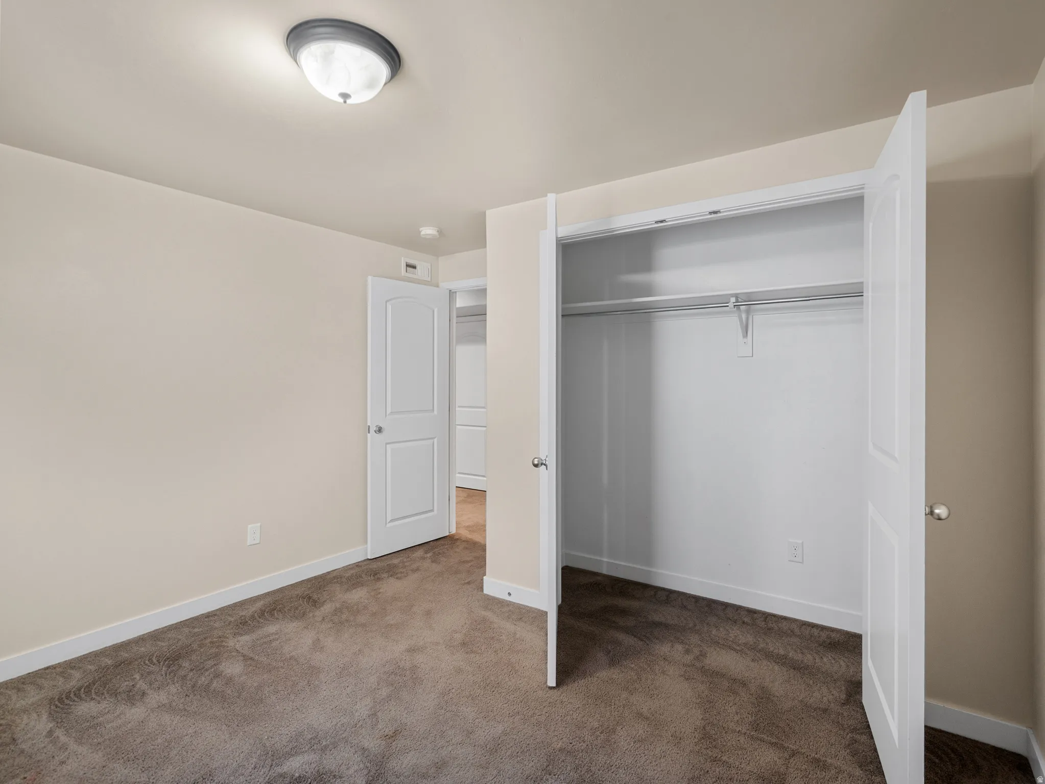 Plush carpet flooring in a neutral tone, ceiling-mounted light fixture, white trim, and a bi-fold closet with an interior hanging rod