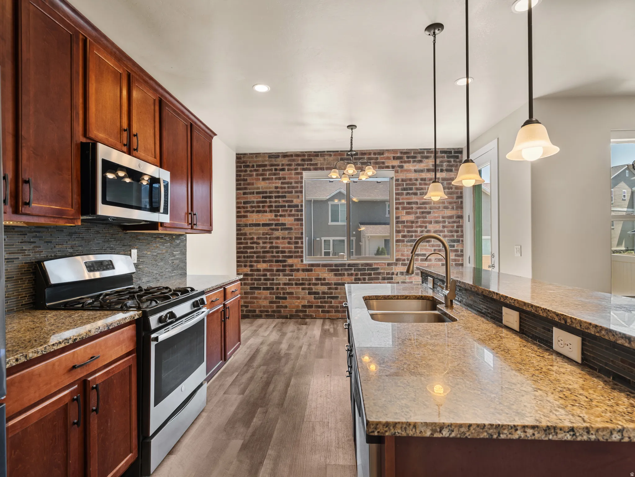 Kitchen featuring rich wood cabinetry, stainless steel appliances, granite countertops, a mosaic tile backsplash, and wood-finish flooring