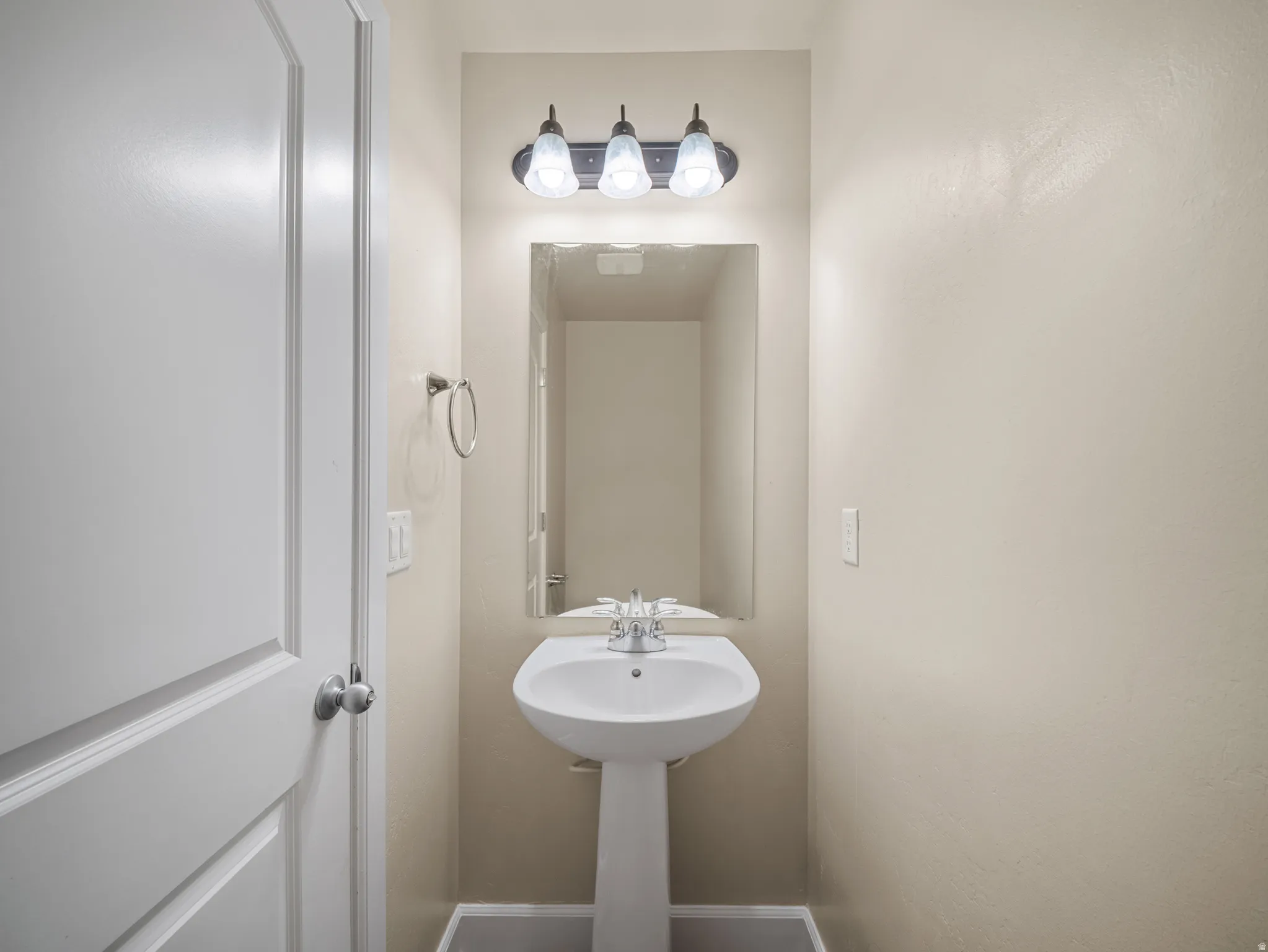 Pedestal sink with chrome faucet, rectangular mirror, and three-light vanity fixture