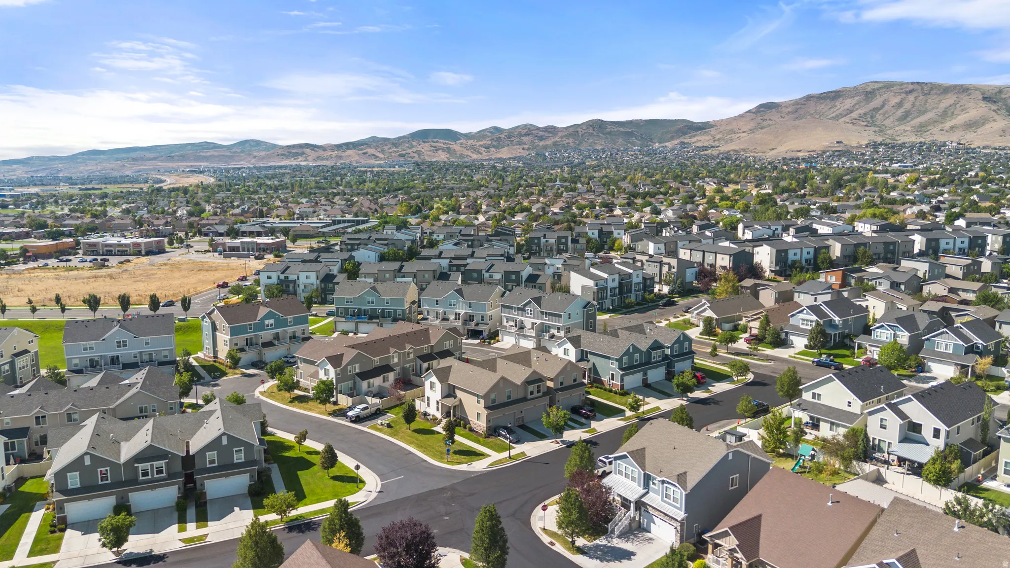 Expansive suburban neighborhood featuring a mix of residential properties, paved streets, and green spaces, all set against a prominent mountain backdrop under a clear blue sky