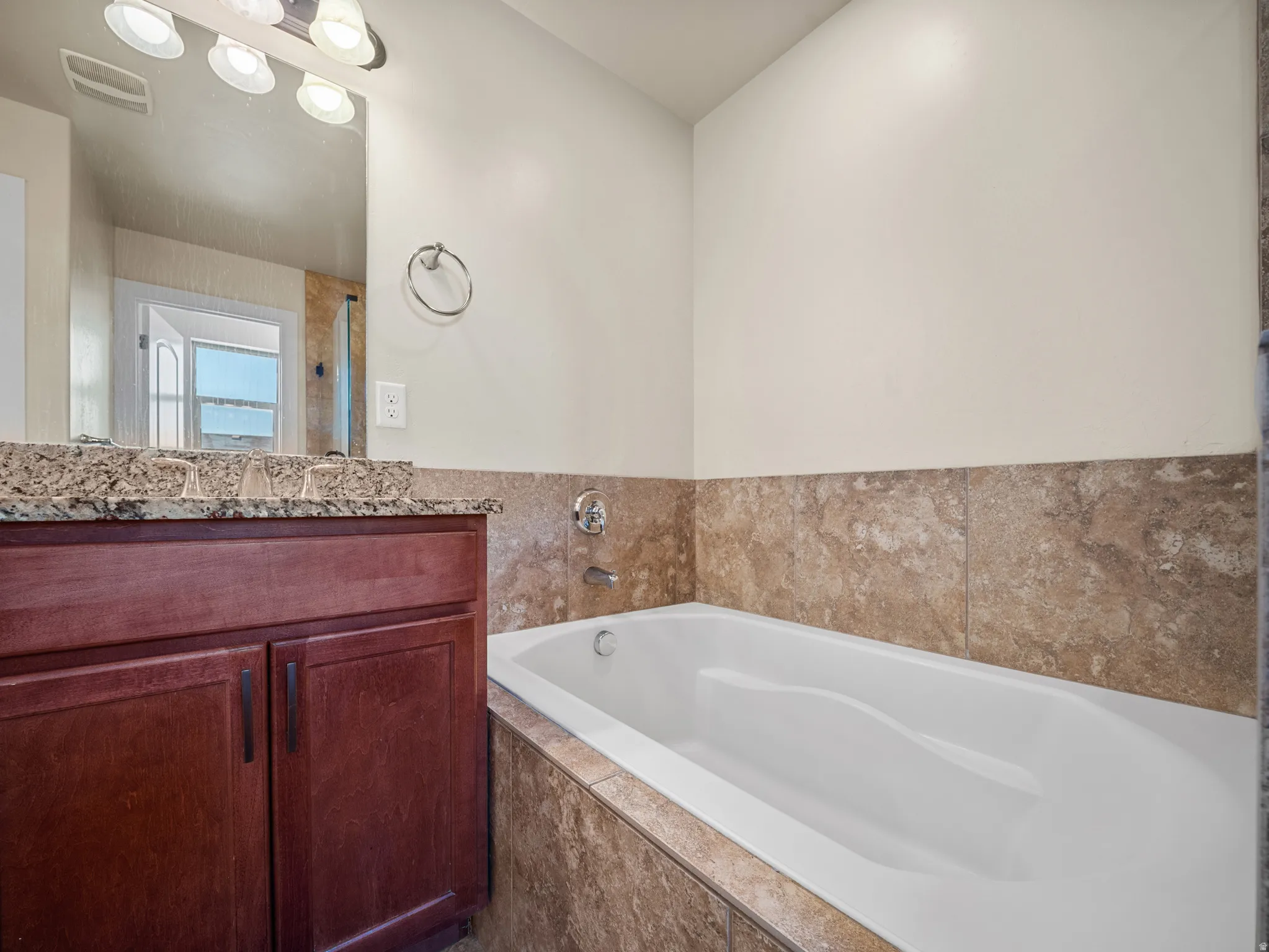 Bathroom featuring a built-in soaking tub, a vanity with a granite countertop, and a tiled tub surround