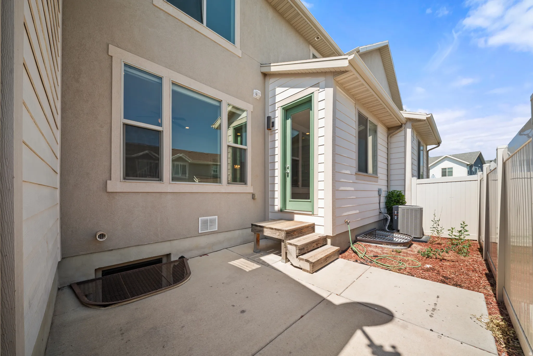 Concrete patio with a basement window well and a side entrance featuring a green door